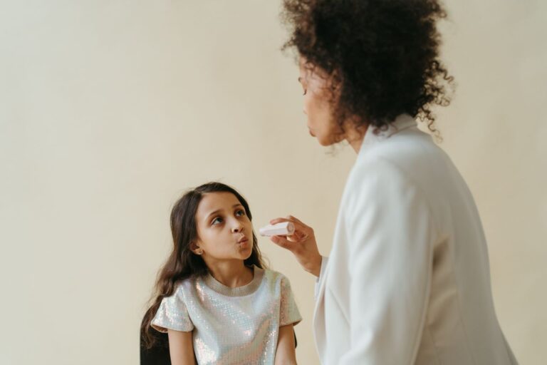 A mother applying makeup to her daughter indoors in a warm, family setting.
